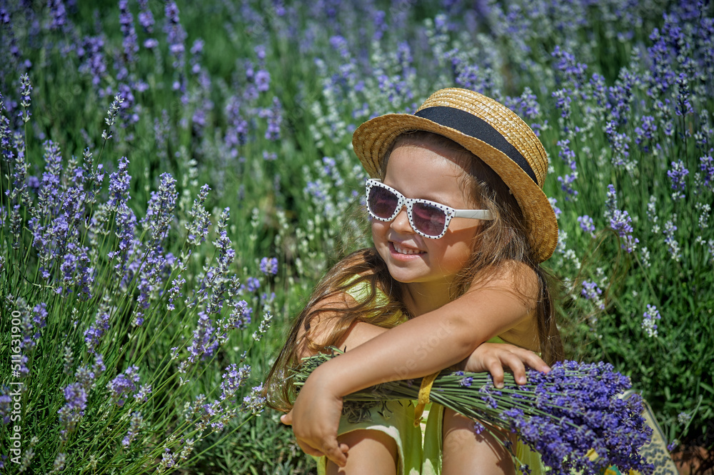 Portrait of a little girl in lavender. Child in a straw hat and sunglasses in nature.
