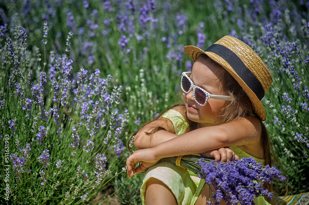 Portrait of a little girl in lavender. Child in a straw hat and sunglasses in nature.