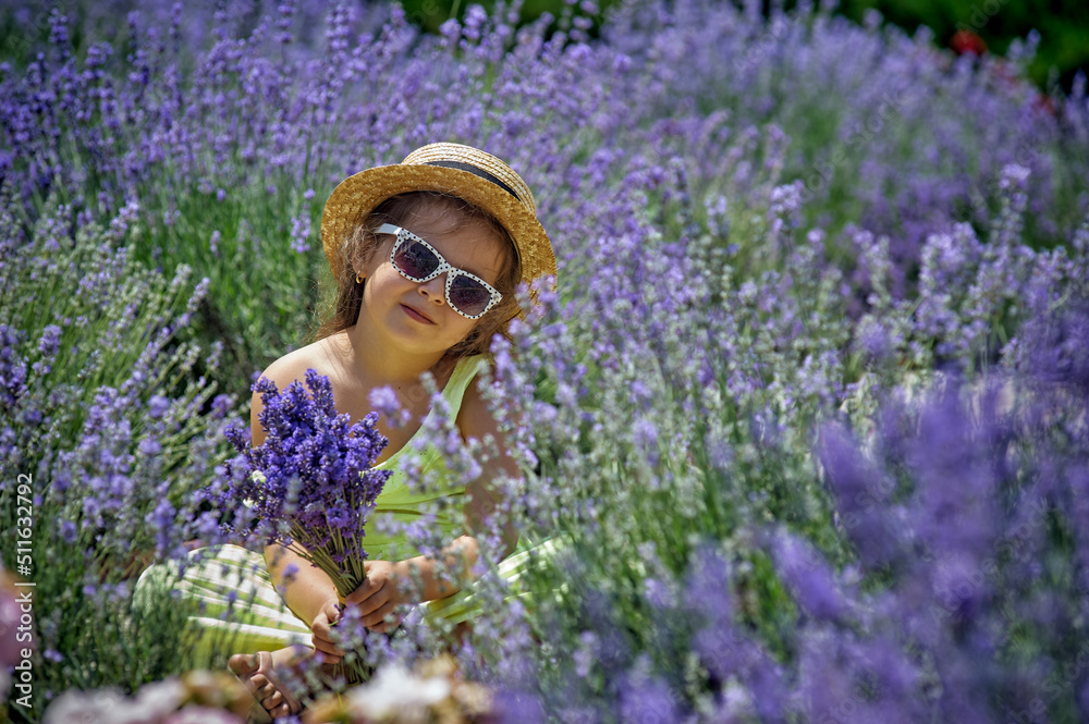 Portrait of a little girl in lavender. Child in a straw hat and sunglasses in nature.