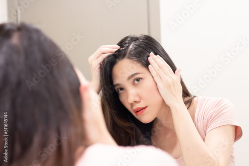 Asian Beautiful woman are looking herself in mirror and use hand touch her hair and looking for grey hair or hair loss with worry face.