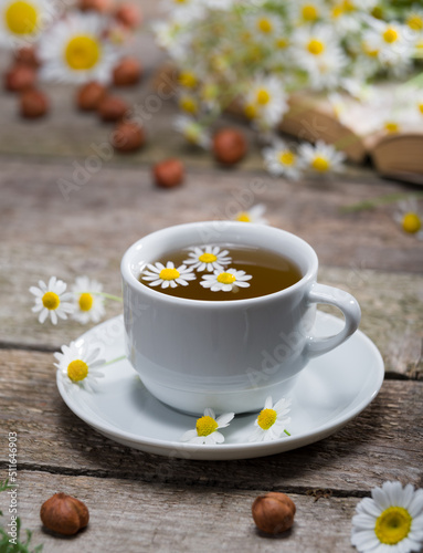 A cup of chamomile tea on the table in the morning light. Herbal tea with book and daisies on wooden rustic table. Vertical view