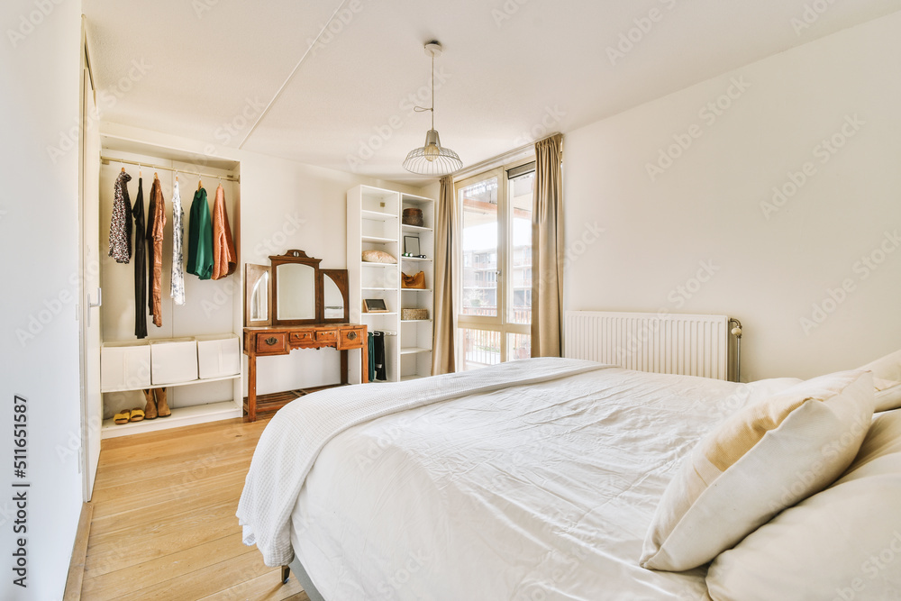 Comfortable bed with white linens opposite dressing table with mirror