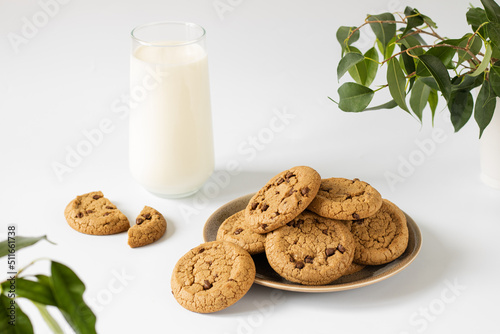 Chocolate chip cookies on a round plate, next to a glass of milk.