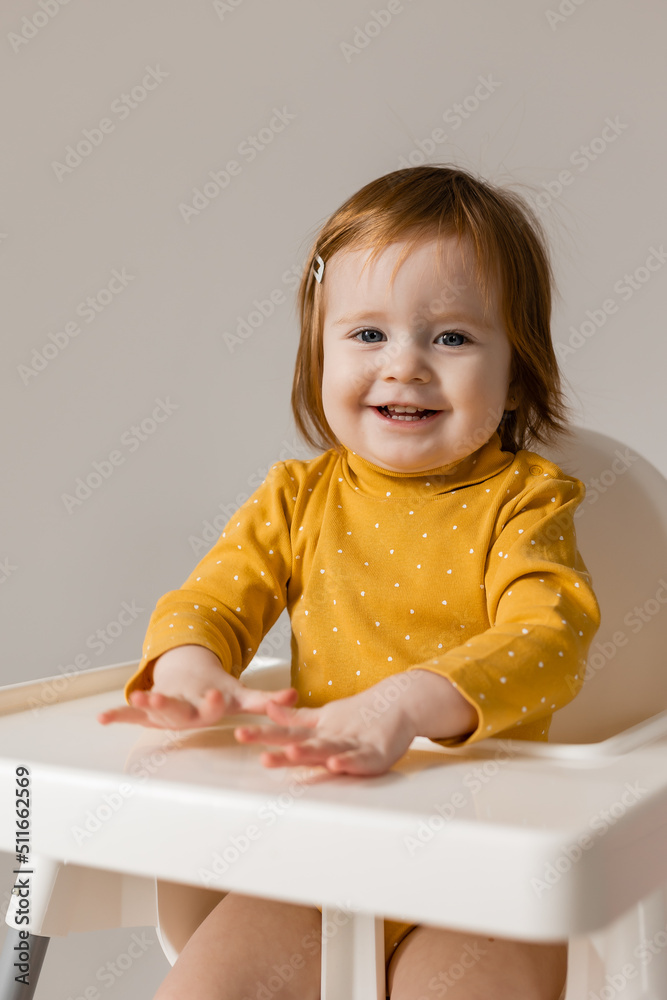 funny red-haired blue-eyed baby in a yellow bodysuit sitting in a white high chair funny red-haired blue-eyed baby in a yellow bodysuit sitting in a white high chair