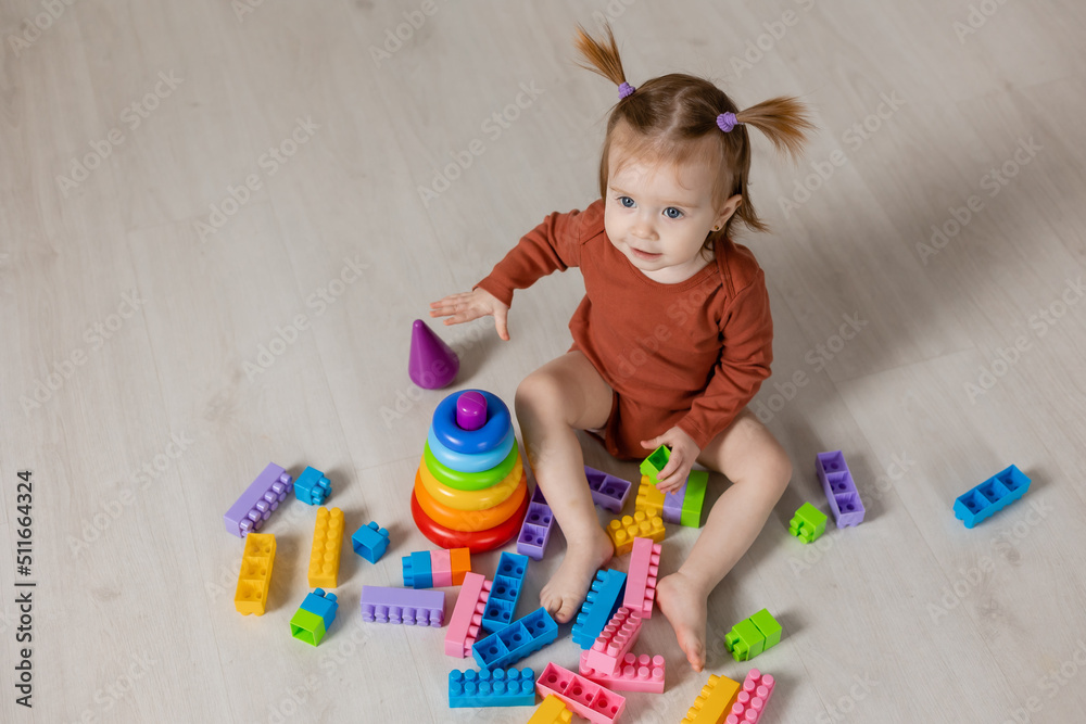 cheerful baby plays with a multi-colored pyramid and other educational toys sitting on the floor