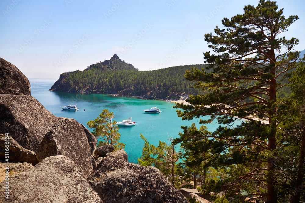 Picturesque seascape. Yachts in a bay with turquoise water color. Around the rocks, huge stones and coniferous forest. 