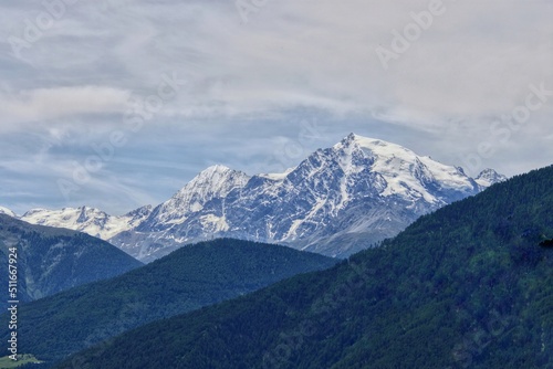 Blick vom Reschenpass auf ein Bergmassiv mit schneebedeckten Gipfeln und Wäldern im Vordergrund