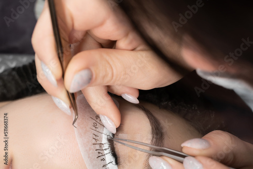 Young woman undergoing eyelash extension procedure using tweezers