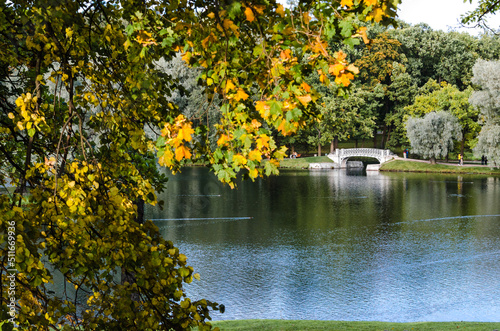 Early autumn, view of the lake with an openwork bridge in a cozy wooded park.