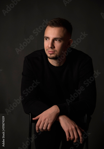 portrait of handsome man sitting on chair in dark studio 