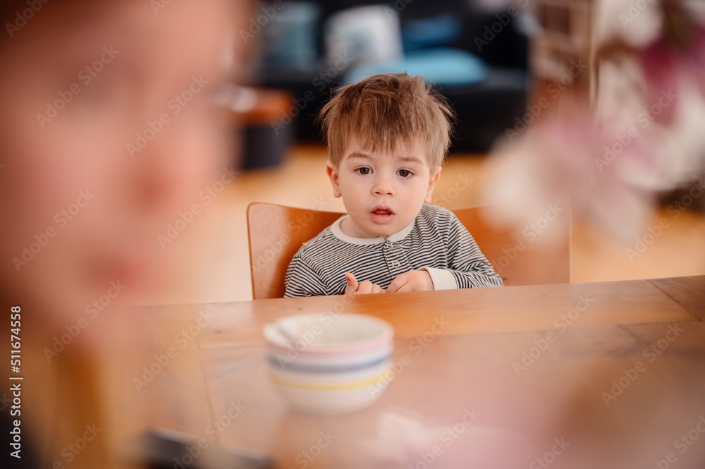 Little emotional toddler boy sitting at a wooden table with deep plate Little emotional toddler boy sitting at a wooden table with deep plate