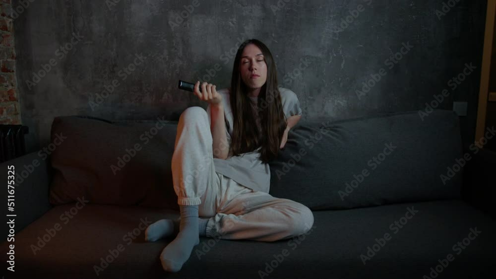 A long-haired brunette is sitting on the couch and switching channels to TV. Home movie viewing A long-haired brunette is sitting on the couch and switching channels to TV. Home movie viewing