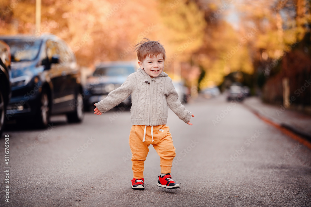 Fototapeta premium Little toddler boy walking down the street in spring-autumn outfit
