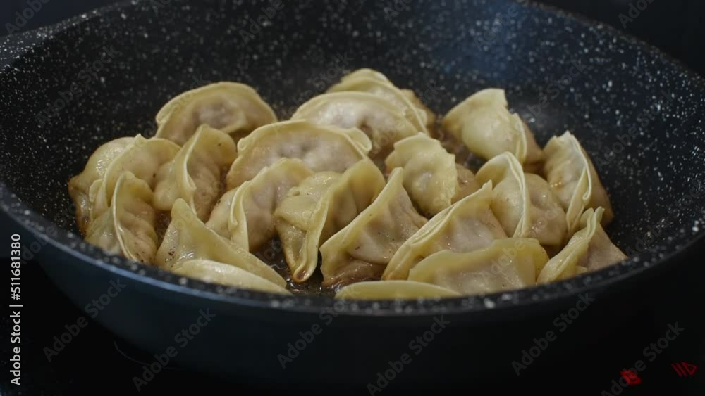 Close up cooking fried dumplings in a frying pan. Chinese food with hot steams.