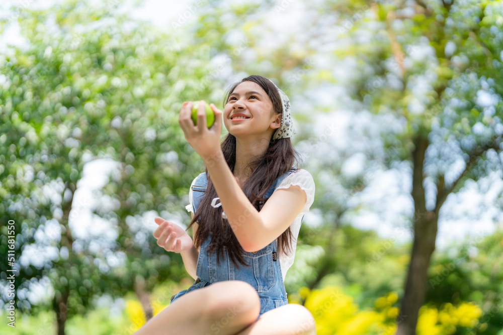 Pretty attractive girl standing in the public garden holding green apple and smile with blur background on sunny day. Happiness during vacation. Relaxation, Aromatherapy freedom feeling lifestyle Pretty attractive girl standing in the public garden holding green apple and smile with blur background on sunny day. Happiness during vacation. Relaxation, Aromatherapy freedom feeling lifestyle
