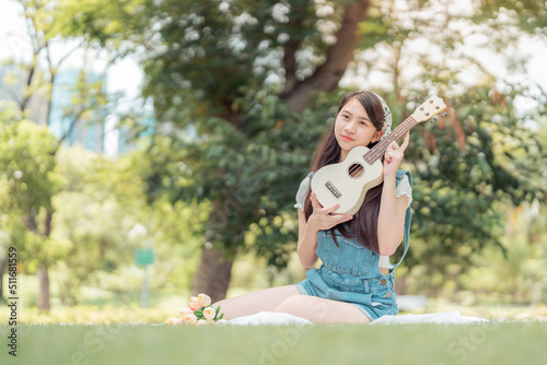 Pretty attractive woman sitting in the garden with blur background. Girl holding Ukulele Guitar on sunny day. Happiness during vacation. Relaxation, Aromatherapy freedom feeling lifestyle