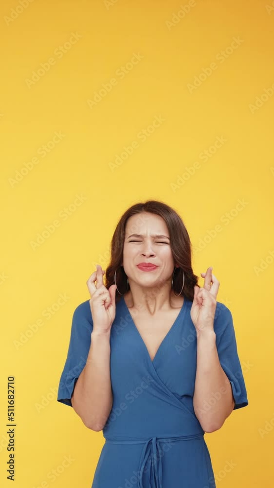 Make a wish. Good luck. Dream hope expectation. Worried excited woman in blue begging with crossed fingers isolated on bright orange vertical empty space background. Make a wish. Good luck. Dream hope expectation. Worried excited woman in blue begging with crossed fingers isolated on bright orange vertical empty space background.