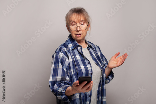 Senior woman in glasses using smartphone over grey background © millaf