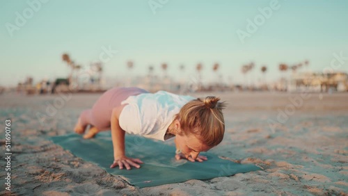 Beautiful shot of sporty woman exercising on yoga mat outdoors. Tattooed girl in sport clothes practicing yoga on the beach
