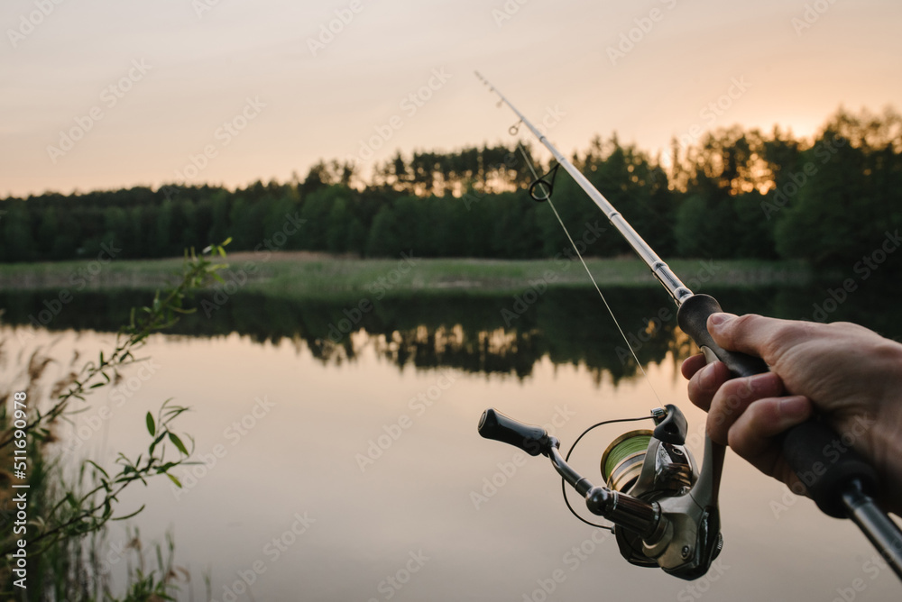 Man catching fish, pulling rod while fishing from lake or pond. Fisherman  with rod, spinning reel