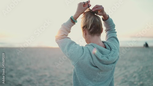 Back shot of sporty woman tying hair in a bun standing on the beautiful beach. Attractive blond girl preparing doing yoga