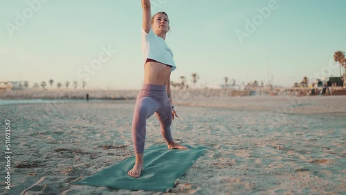 Full length shot of beautiful girl doing yoga on fitness mat on the beach. Attractive woman in sportswear doing stretching workout during yoga class outdoors