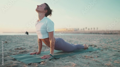 Beautiful woman exercising on yoga mat outdoors. Fitness girl in sport clothes practicing yoga to stay fit. Yoga on the beach