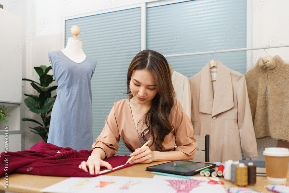 Fashion design concept, Asian female tailor using tape measure on fabric for tailoring new dress Fashion design concept, Asian female tailor using tape measure on fabric for tailoring new dress