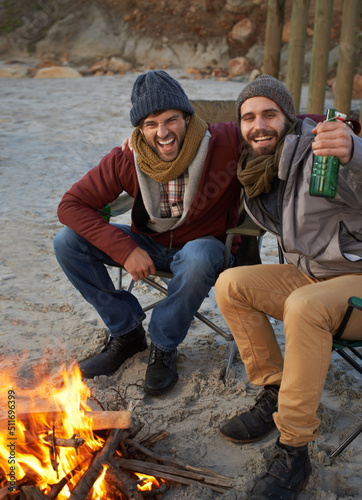 Warming up with a fire and a beer. Two young men sitting around a fire on the beach.