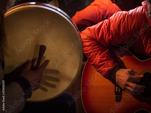 Female bodhrán player and male guitar player with an orange jacket.