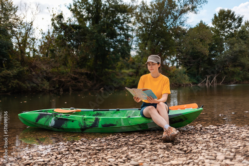 Pretty caucasian young woman is sitting on a kayak, holding a paper map. Copy space. The concept of the World Tourism Day