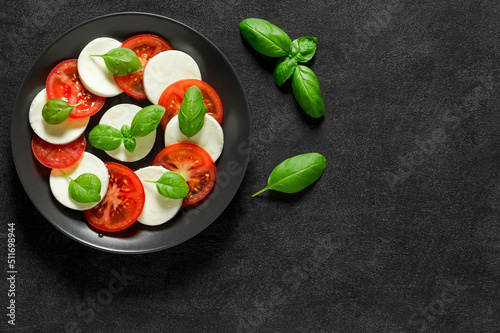 Caprese on plate and basil leaves, on dark background, top view, space to copy text.