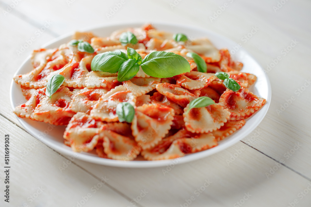Farfalle pasta cooked with tomato sauce and basil, in a white plate, selective focus. Farfalle pasta cooked with tomato sauce and basil, in a white plate, selective focus.