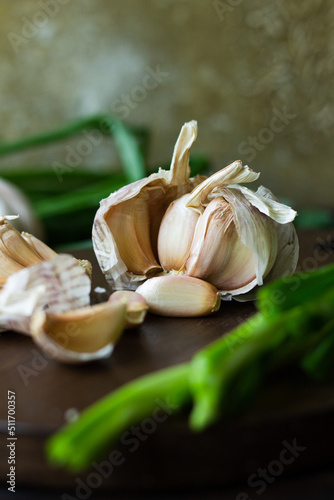 Garlic cloves in composition with green onion on wooden background.