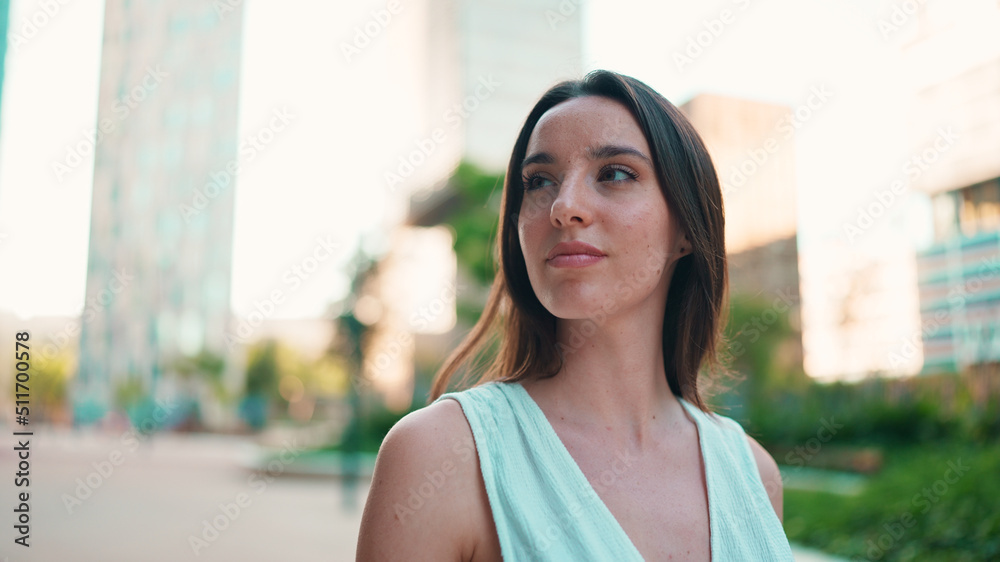 Lovely young woman with freckles and dark loose hair wearing white top and jeans is enjoying the view of modern city. Beautiful girl with long eyelashes looks at the upper floors of building