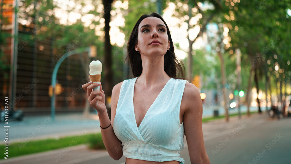 Close-up beautiful woman with freckles and dark loose hair wearing white top testing ice cream. Cute girl enjoys ice cream on modern city background Close-up beautiful woman with freckles and dark loose hair wearing white top testing ice cream. Cute girl enjoys ice cream on modern city background