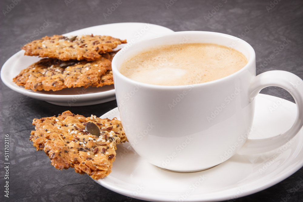 Cup of coffee with milk and fresh baked oatmeal cookies on white plate. Delicious crunchy dessert Cup of coffee with milk and fresh baked oatmeal cookies on white plate. Delicious crunchy dessert
