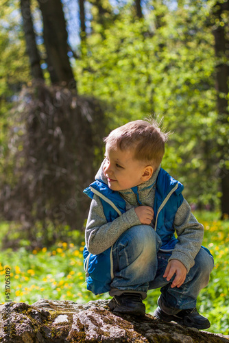 Portrait of a boy in a blue tank top in the woods in spring. Take a walk in the green park in the fresh air. The magical light from the sun's rays falls behind the boy. © Alina Lebed