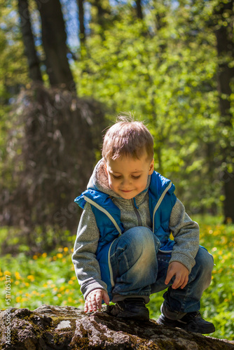 Portrait of a boy in a blue tank top in the woods in spring. Take a walk in the green park in the fresh air. The magical light from the sun's rays falls behind the boy.