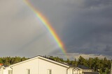 Beautiful view of rainbow in cloudy evening summer sky over suburb houses roofs. Sweden.