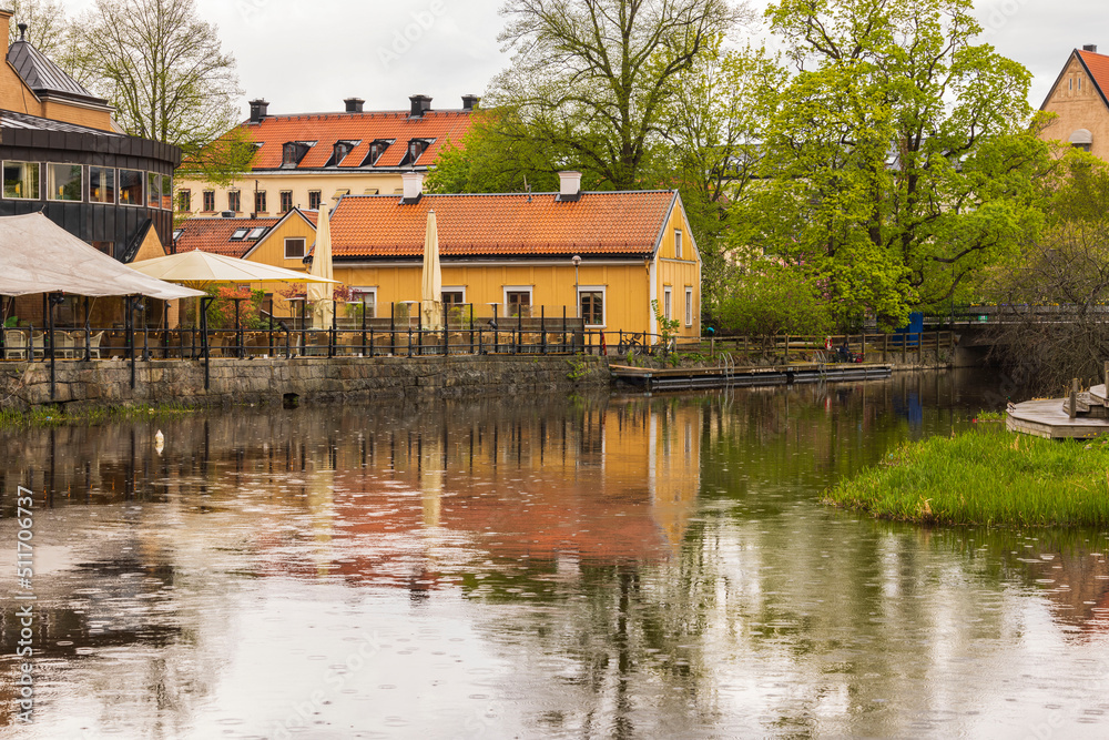 Fototapeta premium Beautiful view of reflection of city houses and trees in clear calm mirror water on rainy summer day. Sweden.