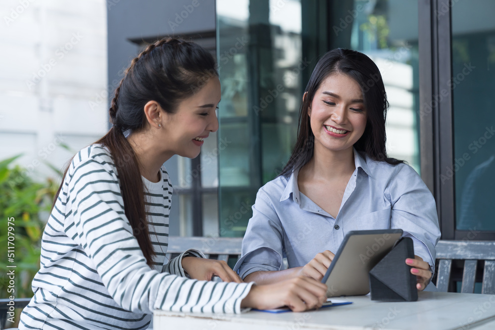 Obraz premium Two Asian young women using digital tablet at the outdoor office. Group of happy asian women colleagues working with tablet outdoor office.