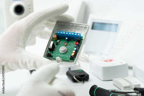 The left hand of a man in a white glove holds a motion sensor of security systems.