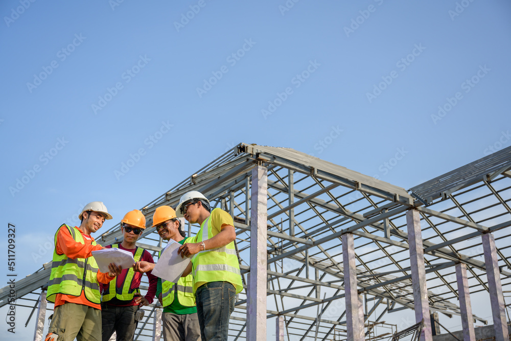 A team of male engineers working at a house construction site. Discuss with the workers and plan the construction of the steel roof truss.