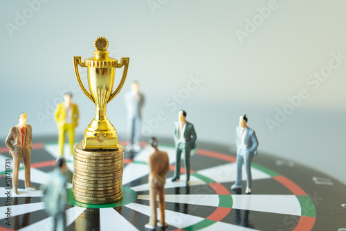 business miniature people standing around gold trophy and stack of gold coin on dartboard hitting in the target center of dartboard  Target business success and investment and finance concepts.