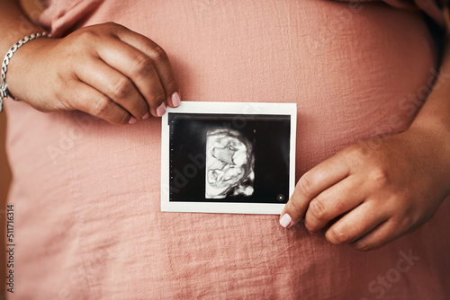 Meet the newest addition to the family. Closeup shot of an unrecognisable woman holding a sonogram in front of her pregnant belly.