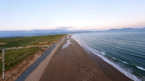 FPV Aerial view of Traeth Llanddwyn Beach at golden hour with snowdon mountains in the far distance slowly climbing altitude with newborough to the left. Northwales UK photo