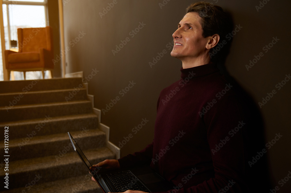 Side portrait of a handsome man working remotely on laptop against dark brown wall background. Businessman, entrepreneur, copywriter, journalist freelance. Online work concept. Copy ad space