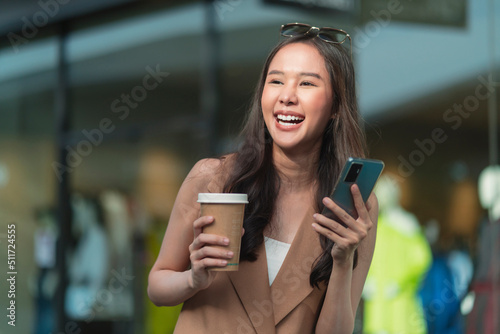 Asian female casual relax digital nomad freelance expat programer smart casual cloth walking on sidewalk urban city with holding smartphone smiling cheerful positive feeling downshifting lifestyle