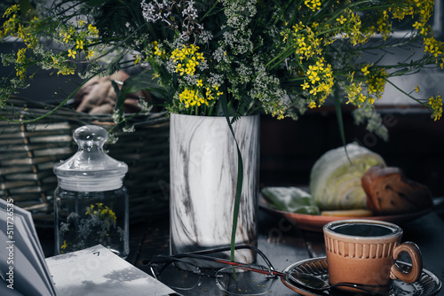 Tableau sur toile bouquet of wild flowers, a mug of cold tea, eyeglasses and notebook on a wooden table at night